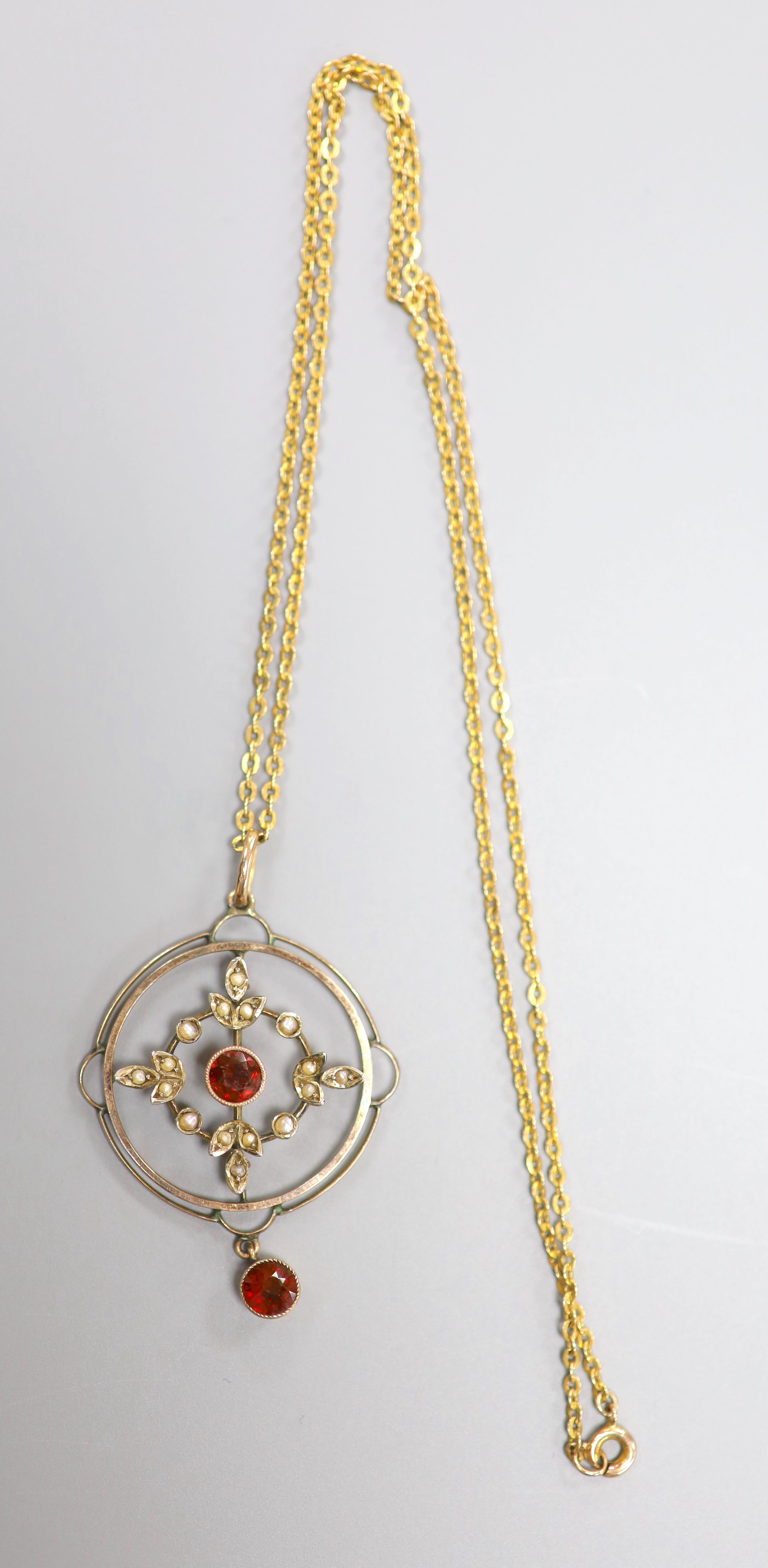 A 9ct, garnet and seed pearl set openwork circular drop pendant, 35mm, on a 9ct chain, 42cm, gross weight 4.9 grams.